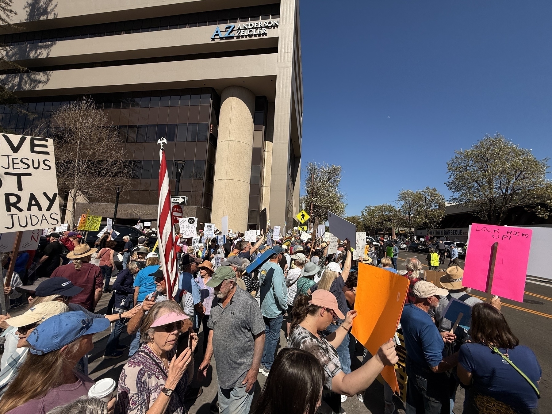 A large group of people is gathered outside a building, holding various signs and participating in a protest or demonstration.