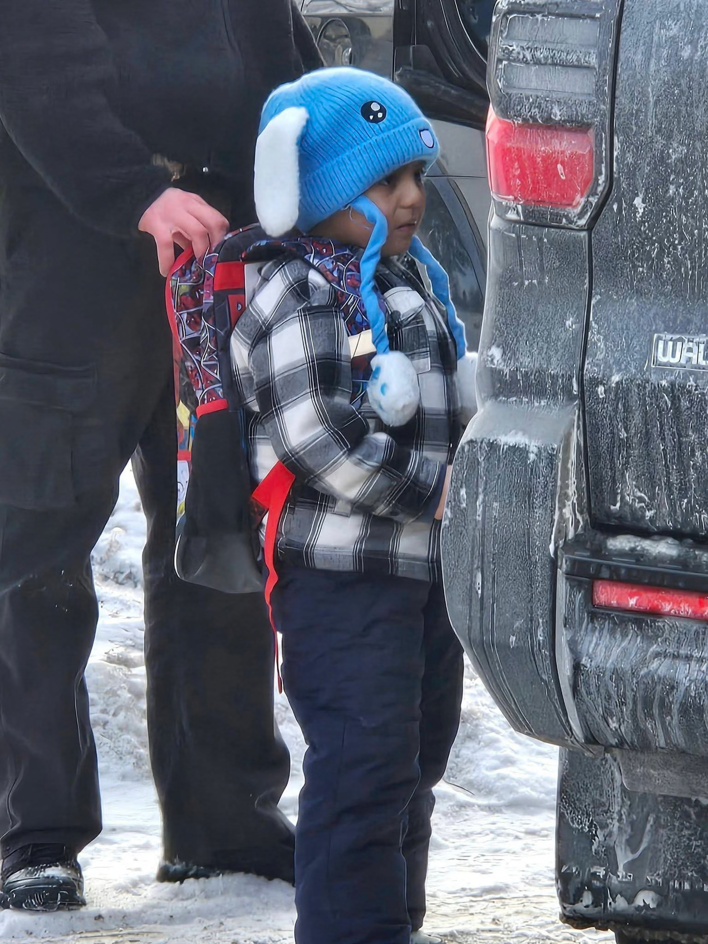 A child in a blue hat with ears and a checkered jacket with a backpack being arrested by ICE. 